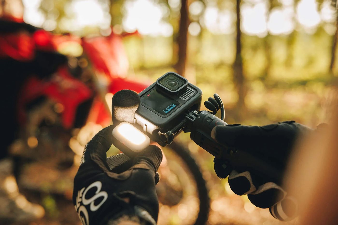 A GoPro with a light and a microphone attached, held on a grip in front of a motocross bike