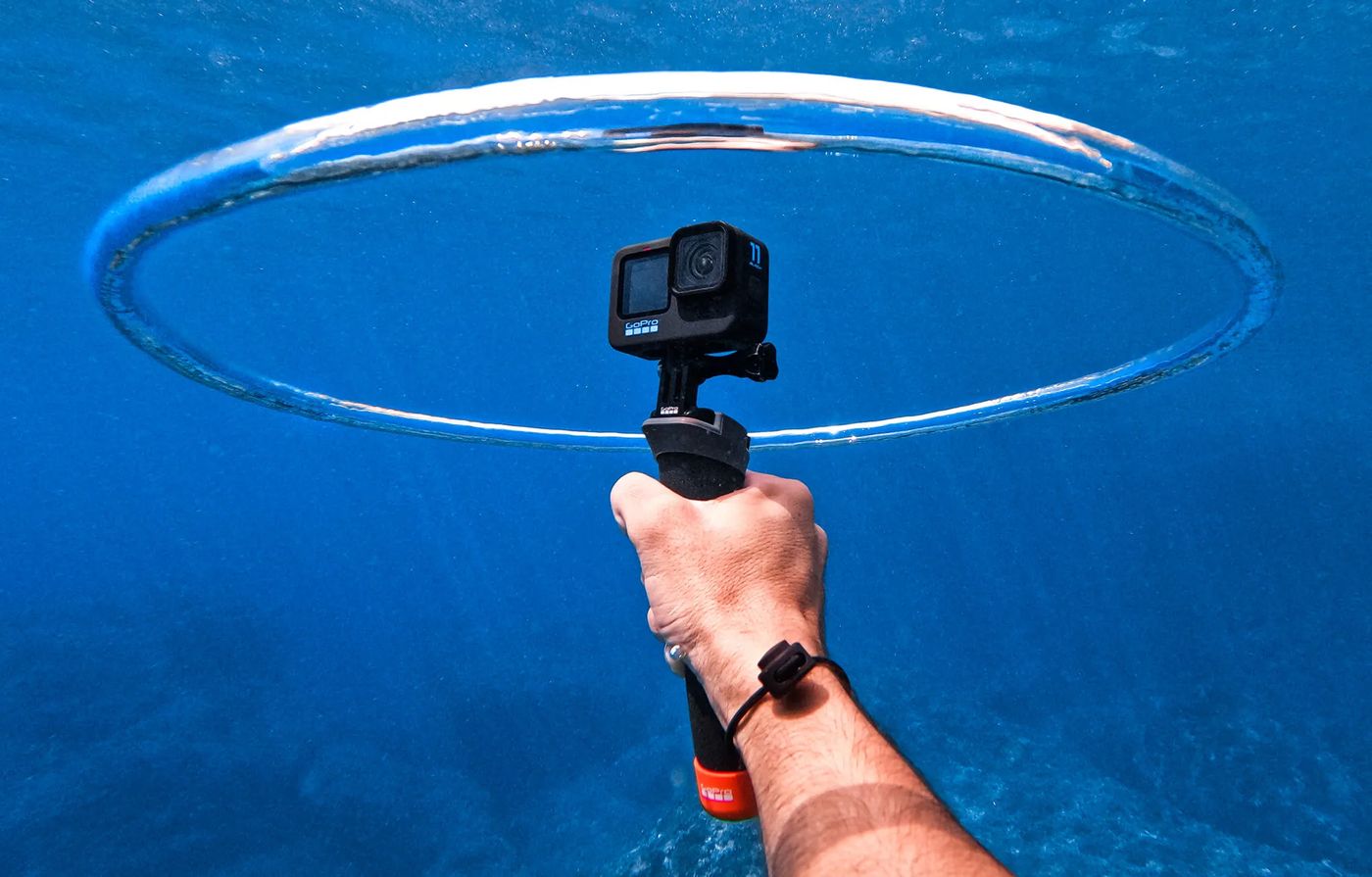 A GoPro on a floating grip underwater, framed by a ring of bubbles