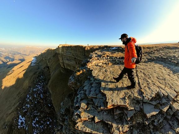 A hiker in a red jacket on a rocky ridge under a bright sky