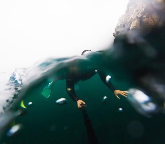 A freediver seen from just under the surface, a camera on a pole in hand